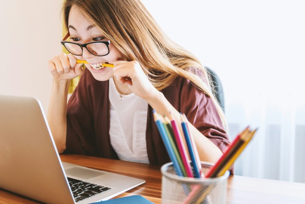 emails woman biting pencil while sitting on chair in front of computer during daytime