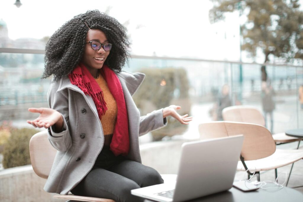 Convert your email list Happy excited African American female laughing and gesticulating while having video calling on laptop and sitting at modern cafe