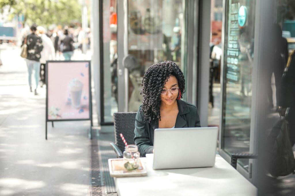 Effective Email List Building High angle of pensive African American female freelancer in glasses and casual clothes focusing on screen and interacting with netbook while sitting at table with glass of yummy drink on cafe terrace in sunny day