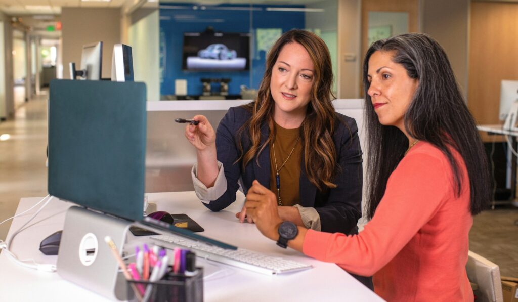 burnout women helping each other two women sitting at a table looking at a computer screen