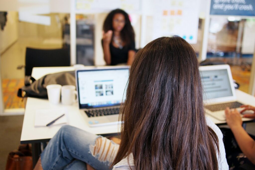 teamwork woman sitting while looking at turned on laptop on tabletop