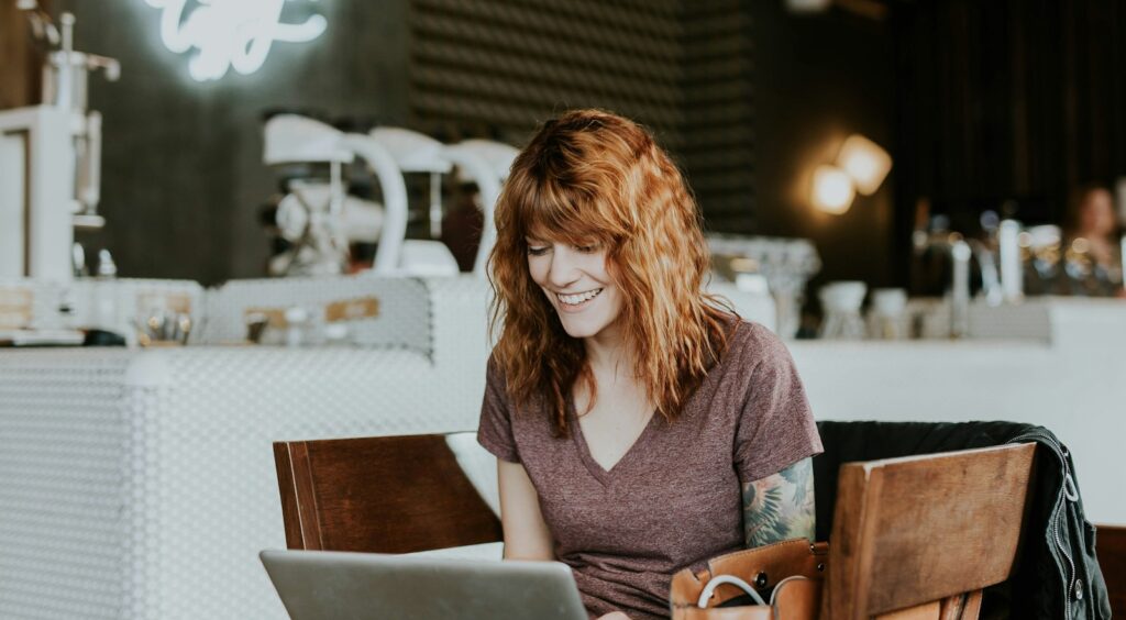 Burnout woman sitting on brown wooden chair while using silver laptop computer in room